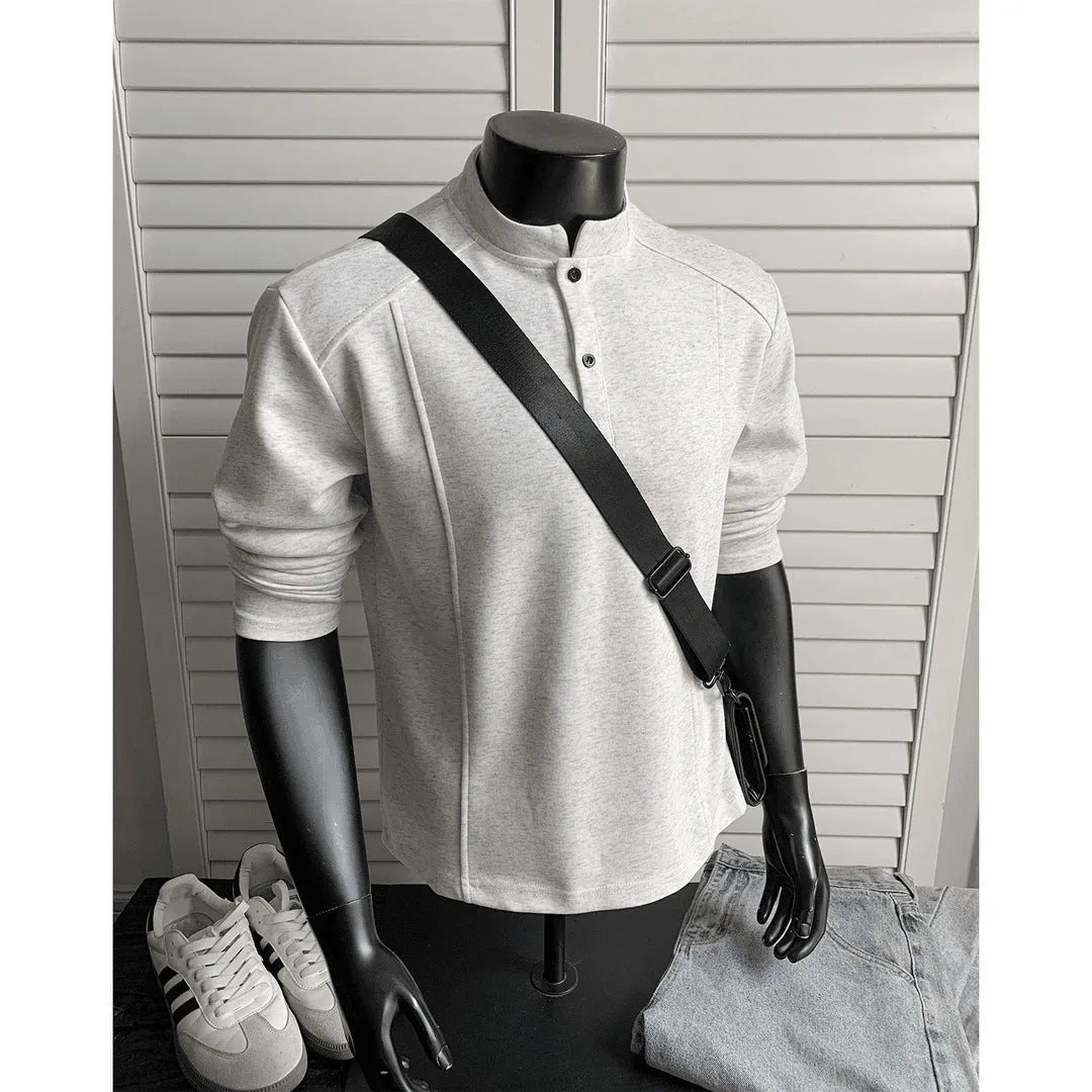 Man wearing a loose fit grey long sleeve sweater with an asymmetric design and a stand-up polo shirt collar.