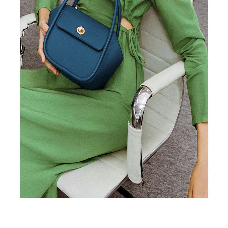 A wing-shaped cow leather tote bag with a buckle latch closure, shown in blue with a single cross-body strap.