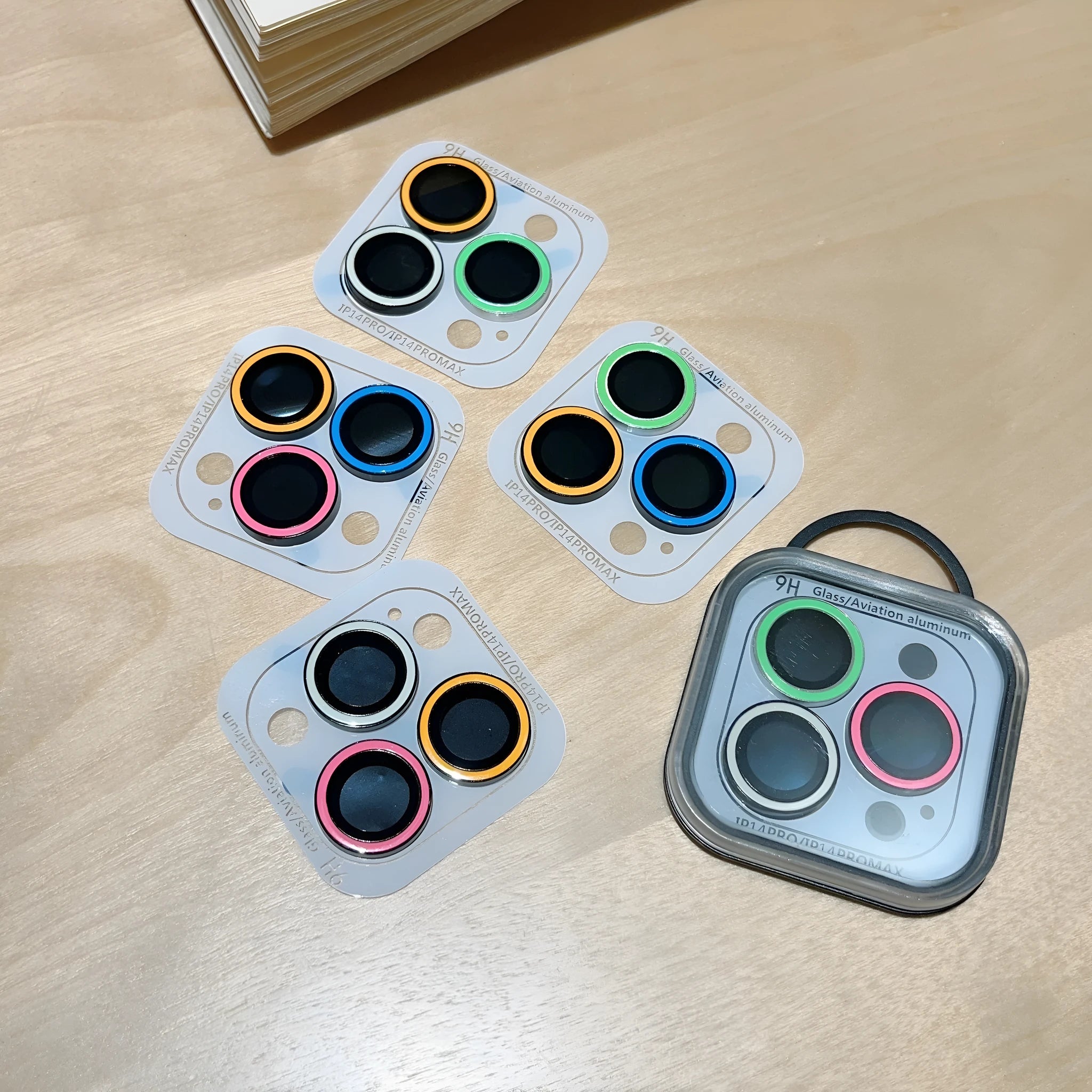 Luminous tempered glass camera lens protector for iPhone 14 Pro Max showing three-hole cutout in yellow blue pink