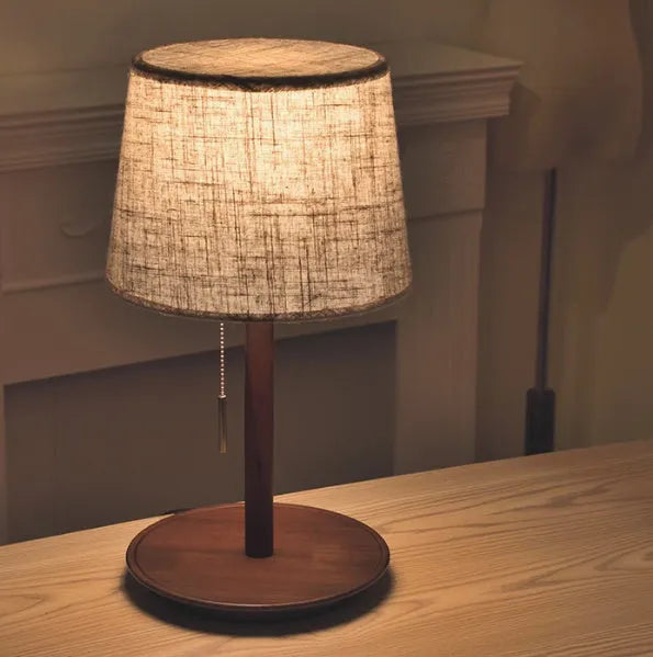 Walnut-coloured solid wood desk lamp with a white fabric shade on a wooden table.