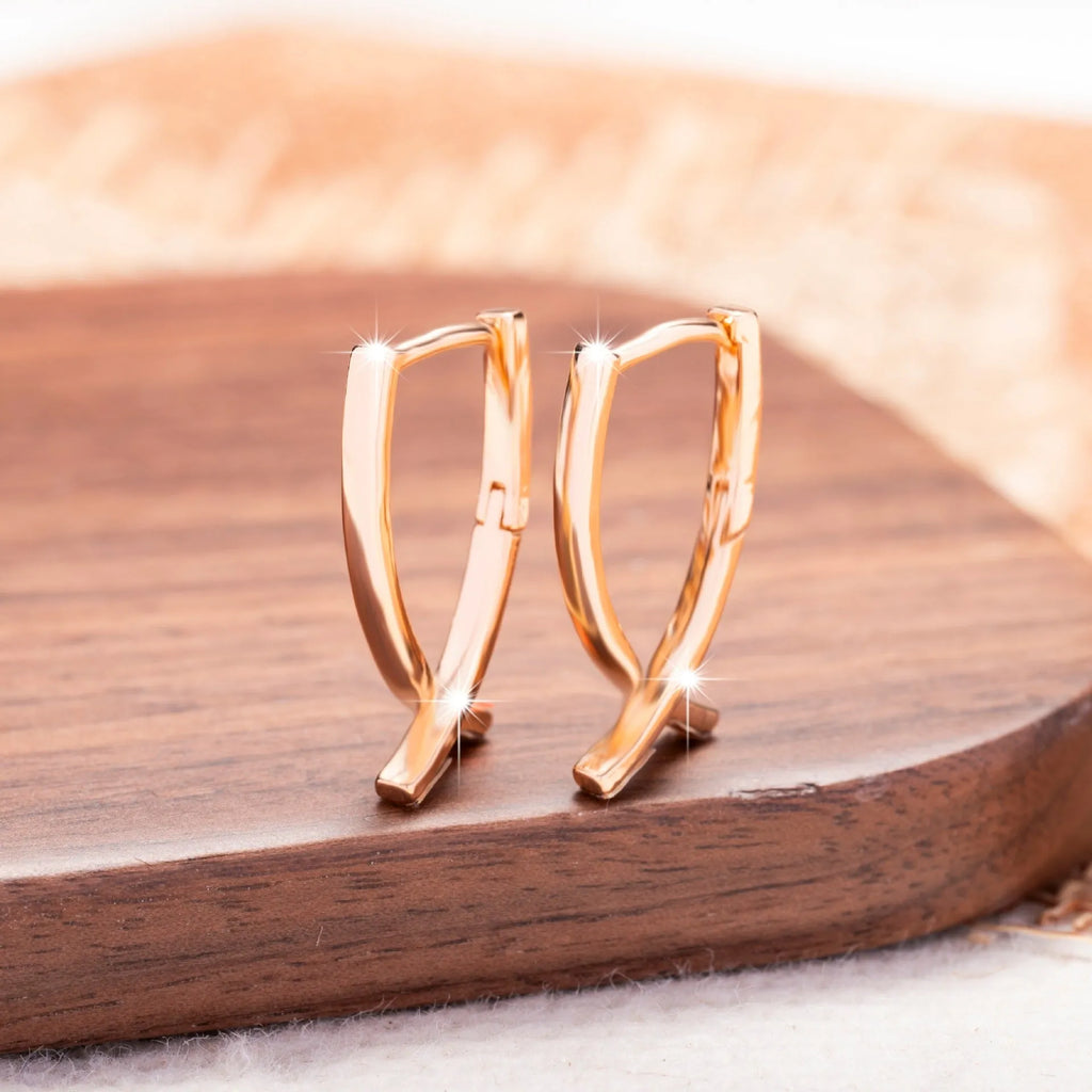 Rose gold coloured cross-shaped earrings on a plain background.