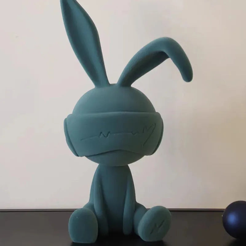 Suede blindfold rabbit resin ornament in green, blue, or red colours on a shelf.
