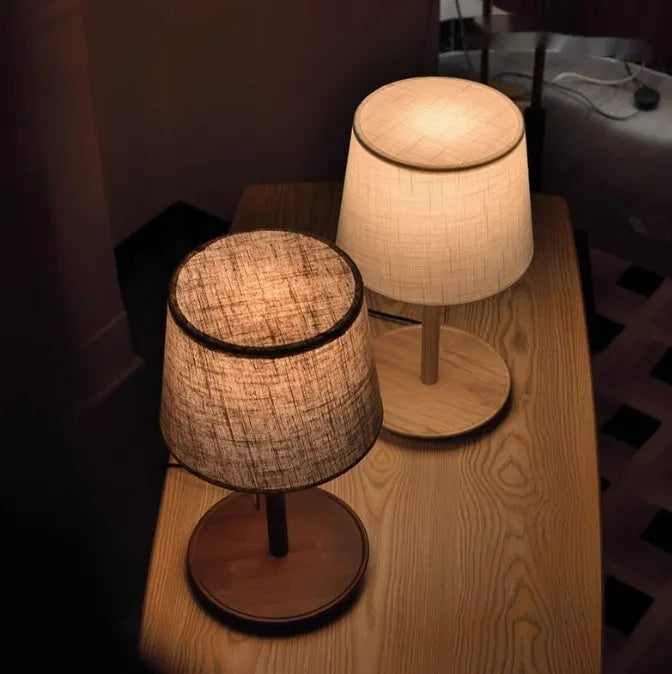 Walnut-coloured solid wood desk lamp with a white fabric shade on a wooden table.
