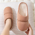 A pair of blue down cotton slippers with a thick rubber sole and artificial leather upper on a wooden floor.