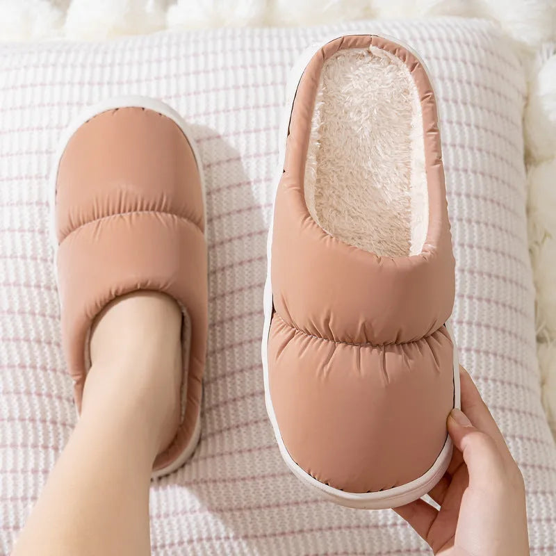 A pair of blue down cotton slippers with a thick rubber sole and artificial leather upper on a wooden floor.