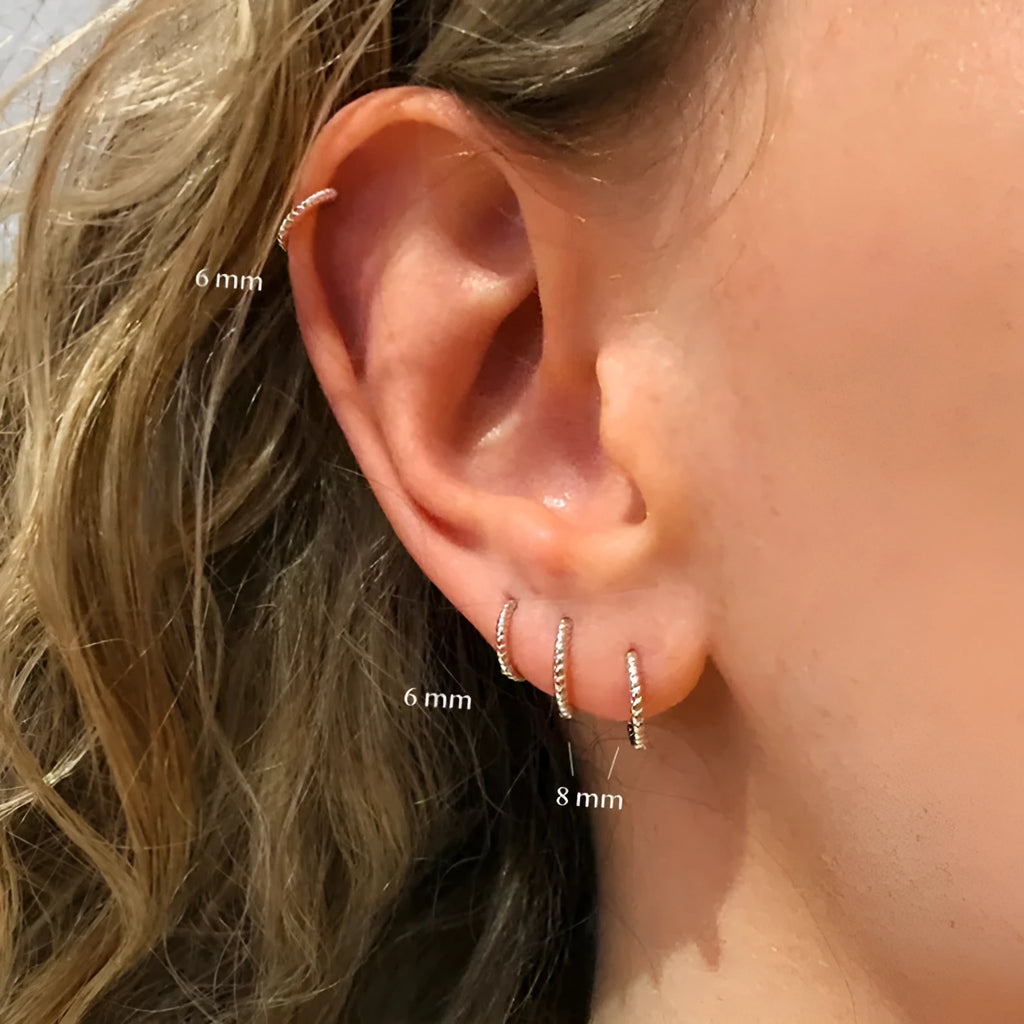 Twisted round sterling silver hoop earrings in golden and white gold colours on a plain background.
