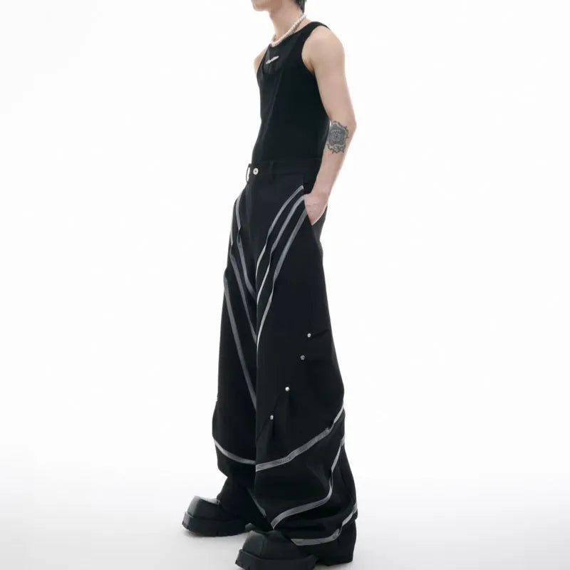 Men's black trousers with three-dimensional cut, metal striped rivet details and pleats on a white background.