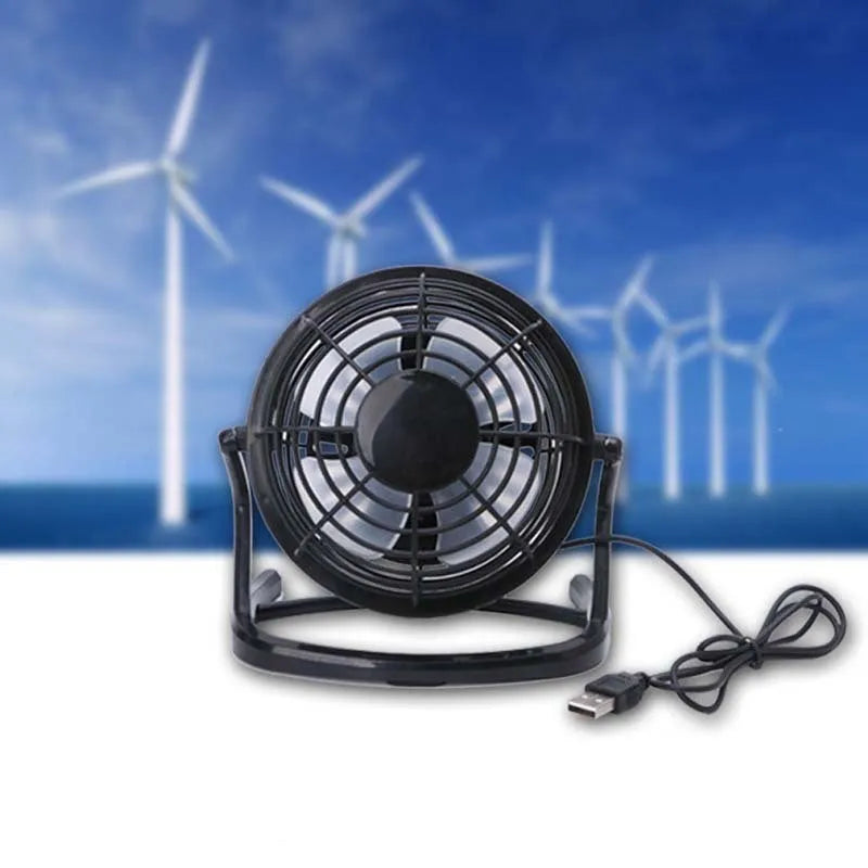 Mini black USB desk fan on a table next to a laptop, showing adjustable tilt angle.