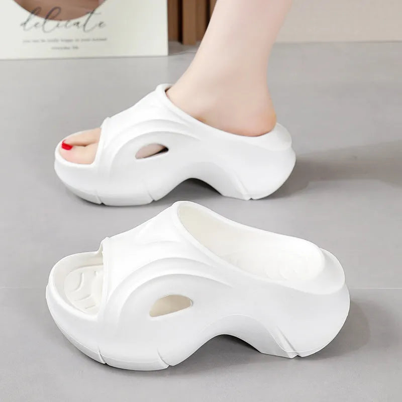White women's EVA slippers with thick sole and round toe on a beach background.