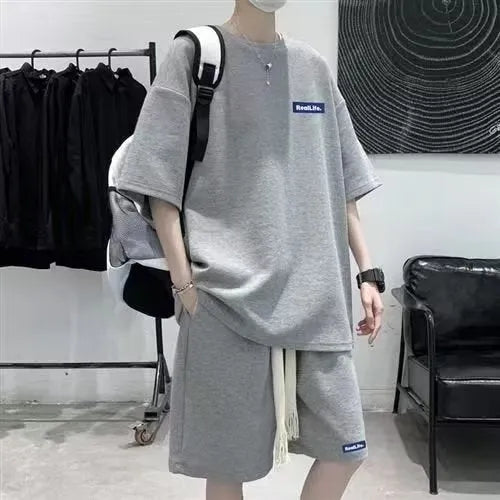 Man wearing a grey waffle-textured short sleeve top and matching shorts from the leisure sports suit set.