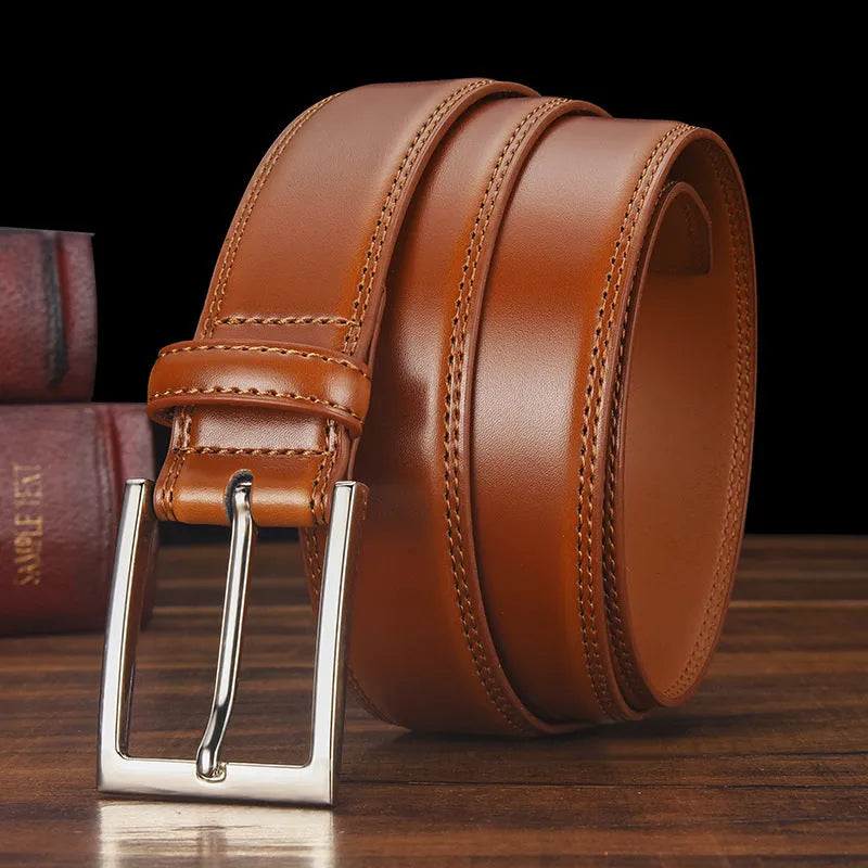 Men's classic black genuine leather belt with a silver-toned alloy pin buckle on a flat surface.