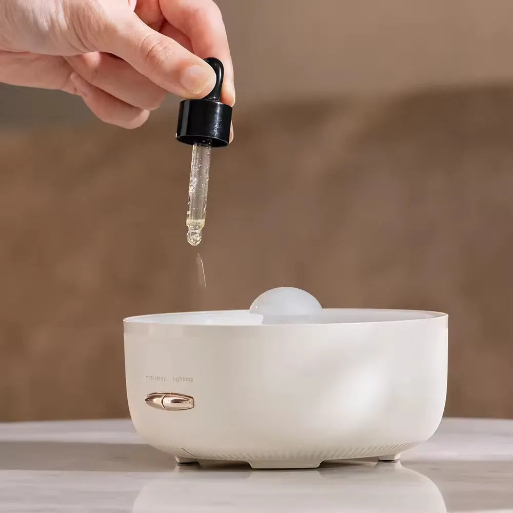 Round resin aroma diffuser in beige on a desk, with mist rising from single outlet, plug-in cord visible