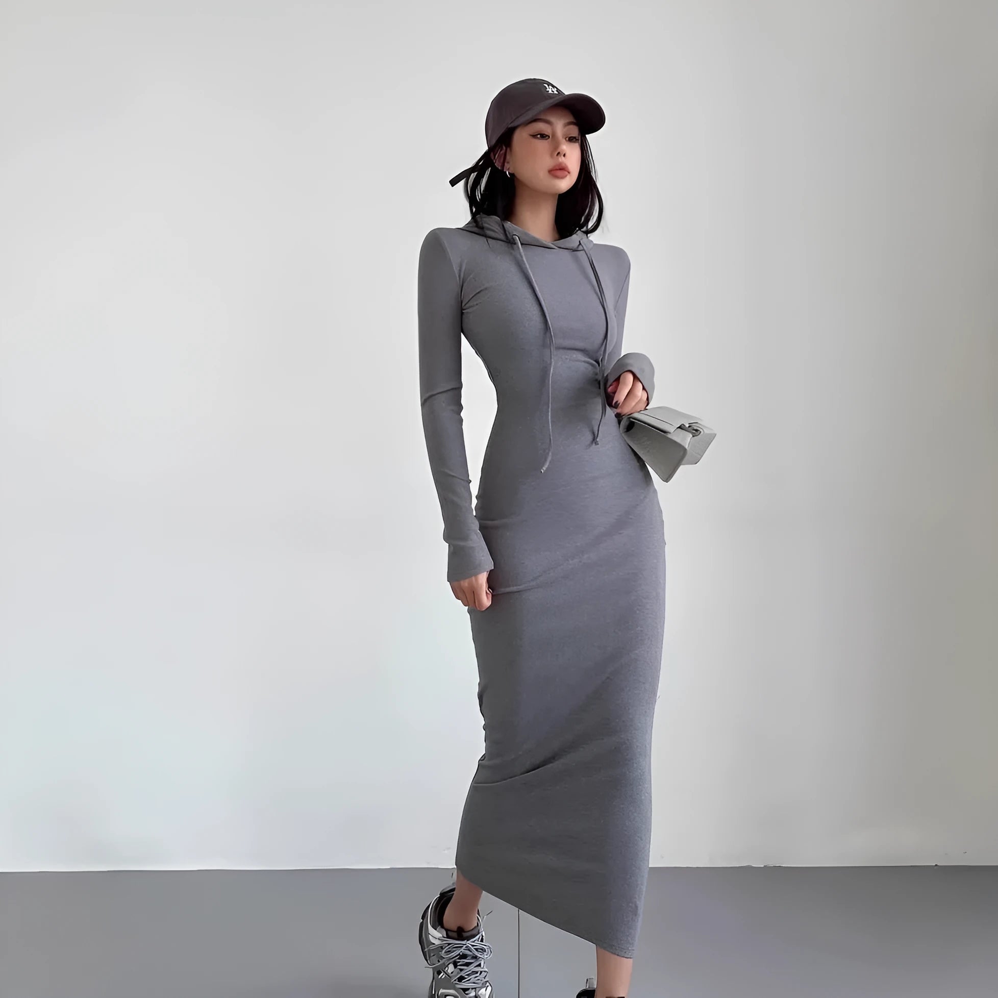 A woman wearing a grey hooded sheath dress with long sleeves and an over-the-knee length.