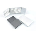 Black tri-fold portable Bluetooth keyboard shown open next to a smartphone, demonstrating its compact size.