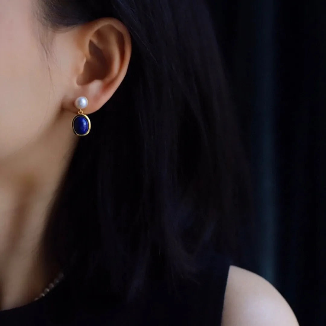 A pair of simple silver drop earrings with blue lapis lazuli pearls and auspicious pattern detailing.