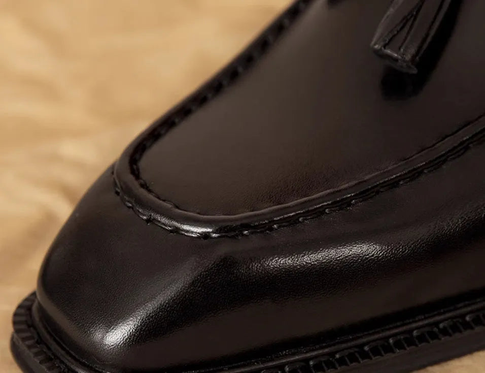Men's black genuine leather slip-on loafers with fringed detailing and a rubber sole, shown from a side view.
