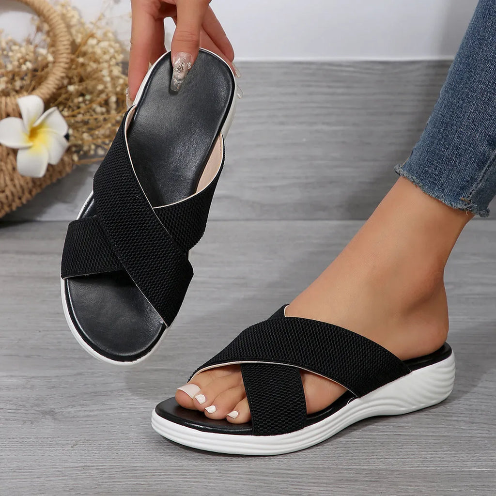 Women's black flat wedge slippers with peep toe and cross strap on a rubber sole.