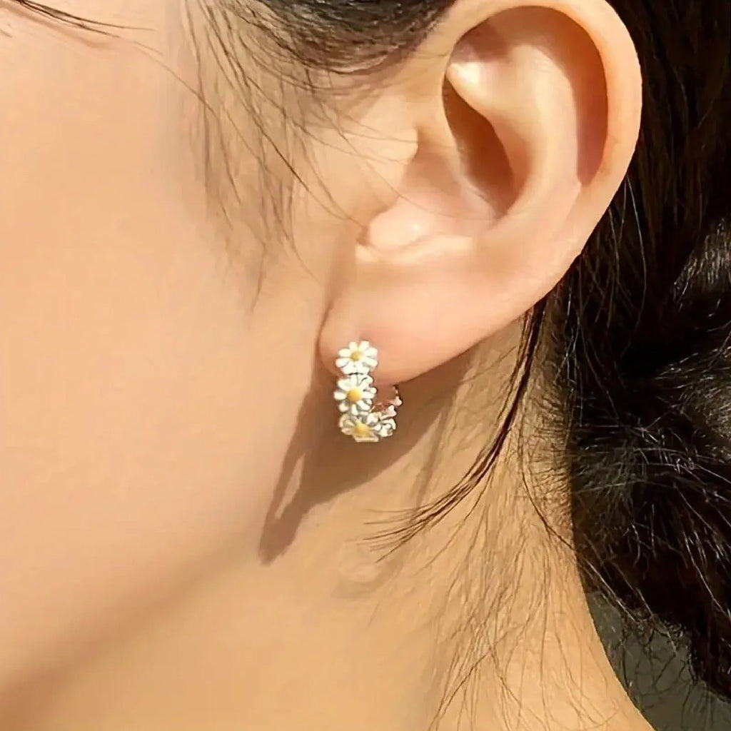 Close-up of white daisy flower ring earrings with gemstone centre on copper setting.