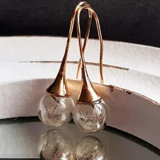 Transparent glass ball earring on a silver French hook, showing a dandelion seed design inside the sphere.