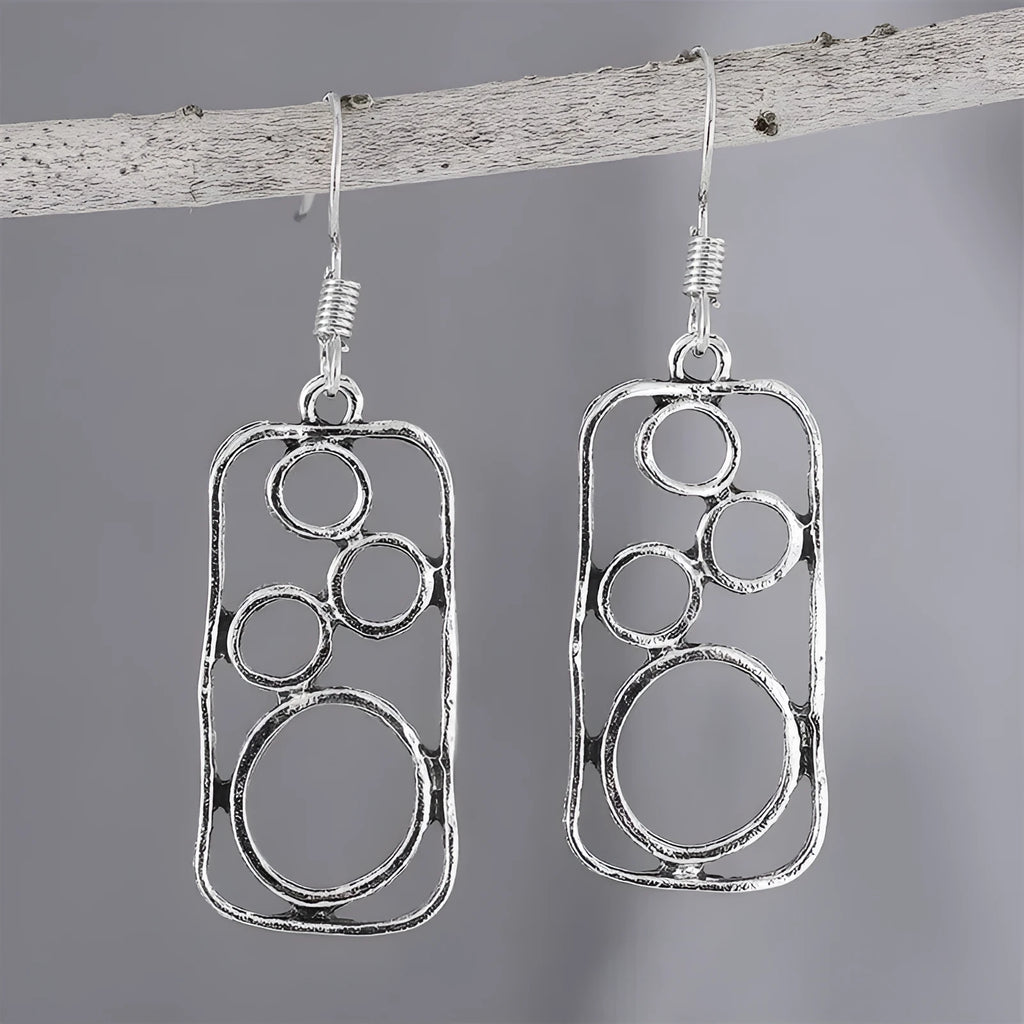 A pair of antique silver geometric earrings showing an irregular square shape inside a round ring.