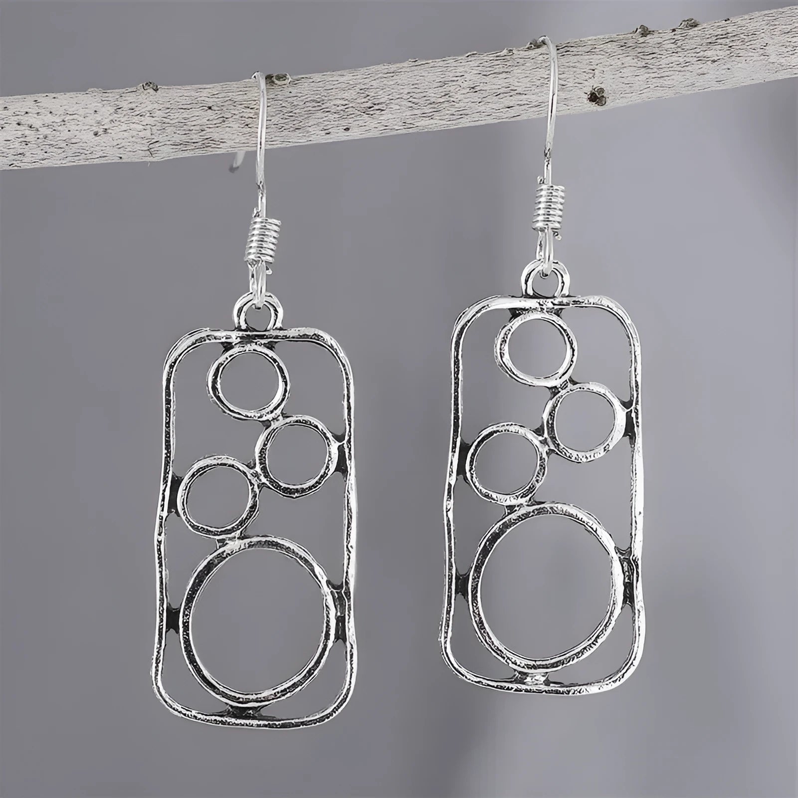 A pair of antique silver geometric earrings showing an irregular square shape inside a round ring.