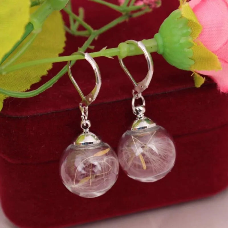 Transparent glass ball earring on a silver French hook, showing a dandelion seed design inside the sphere.