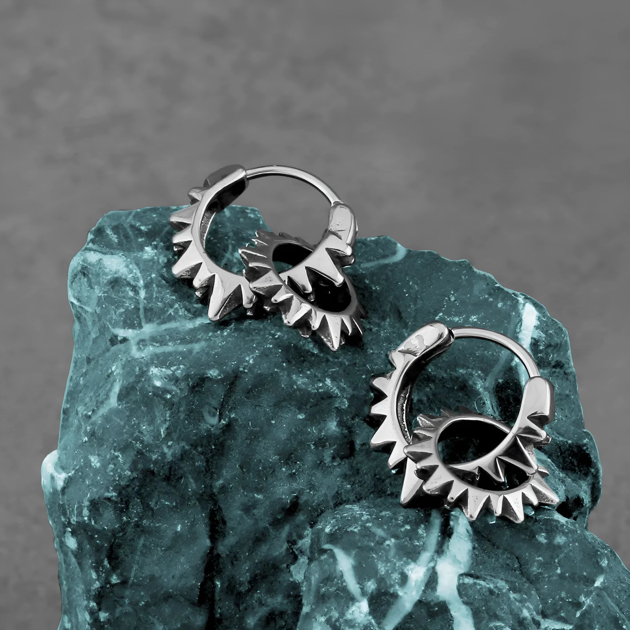 A pair of polished stainless steel round ring earrings in a retro style on a steel colour background.