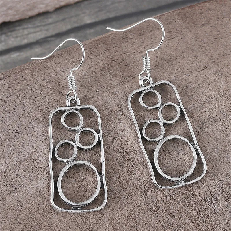 A pair of antique silver geometric earrings showing an irregular square shape inside a round ring.