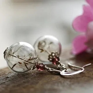 Transparent glass ball earring on a silver French hook, showing a dandelion seed design inside the sphere.