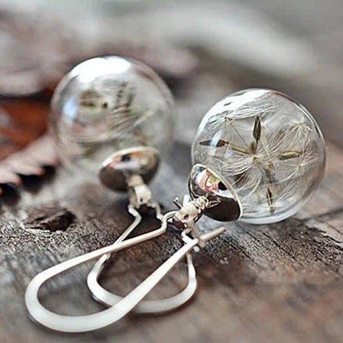 Transparent glass ball earring on a silver French hook, showing a dandelion seed design inside the sphere.
