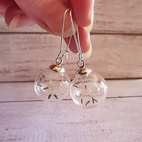Transparent glass ball earring on a silver French hook, showing a dandelion seed design inside the sphere.