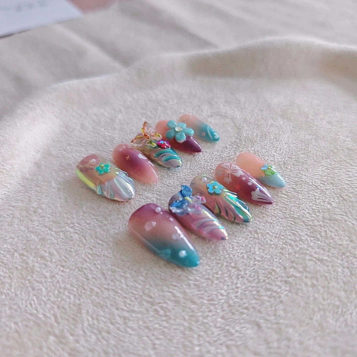 Handmade three-dimensional flower and butterfly nail art sculptures in assorted sizes on a manicure set.