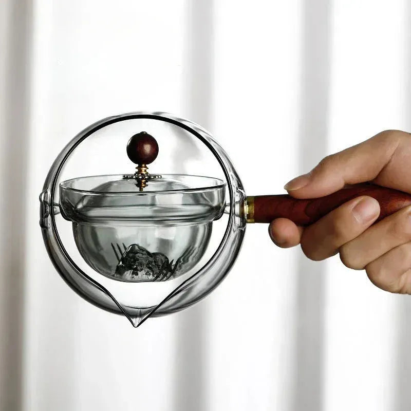 Semi-automatic rotary heat-resistant glass teapot with infuser and wooden handle on a table, transparent or grey