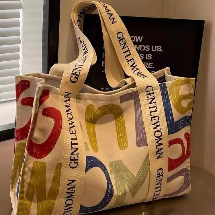 Large canvas tote shoulder bag with printed design in black letter, coloured letter, and pattern styles.