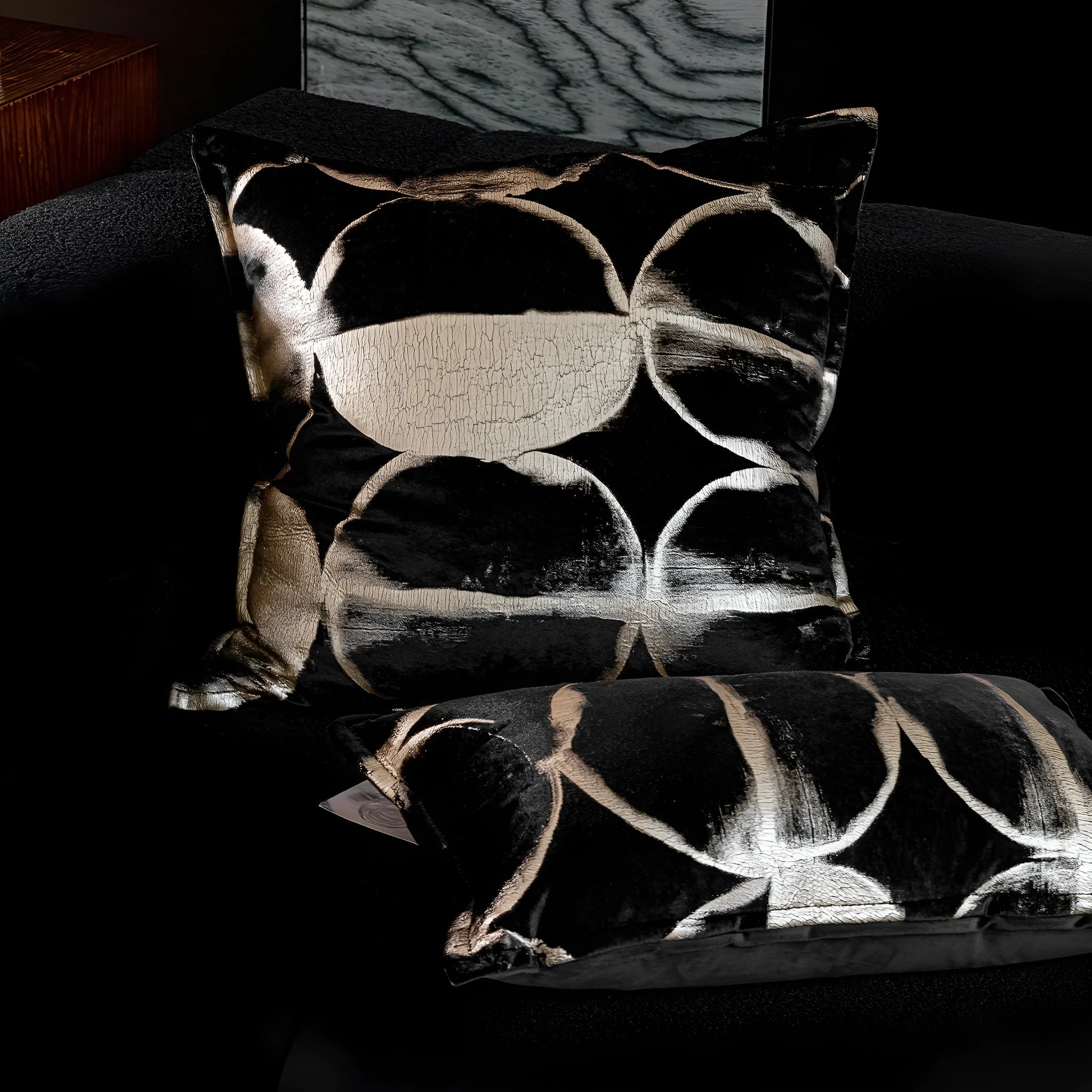 Black and gold abstract pattern flannel pillow cover on a grey sofa.