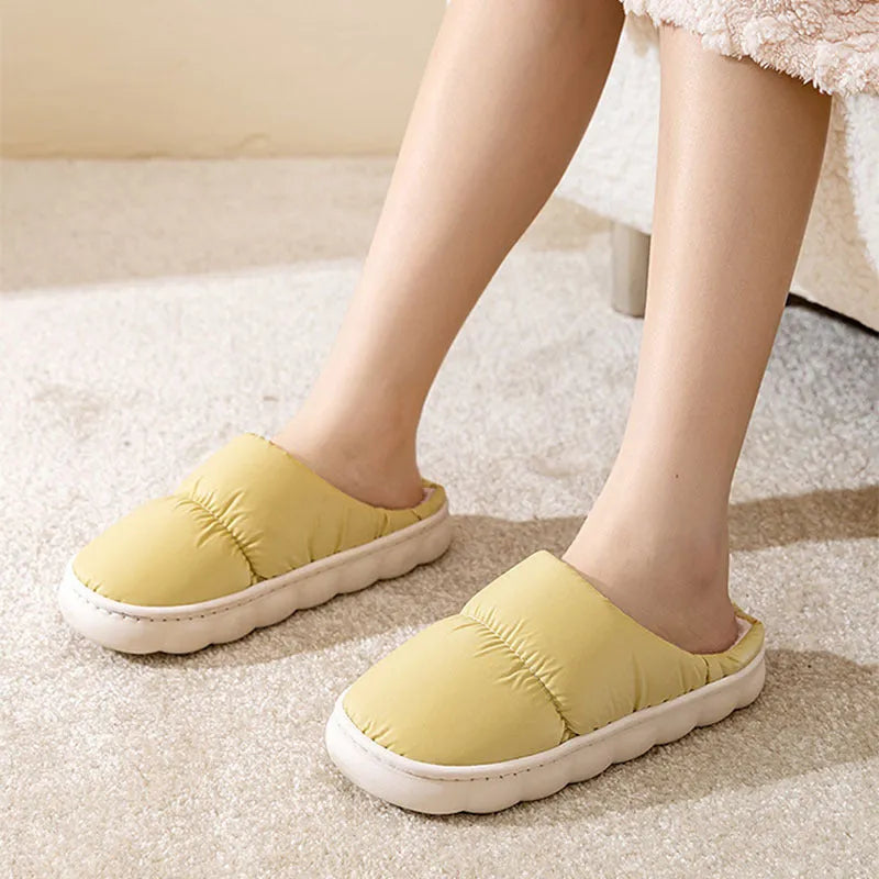 A pair of blue down cotton slippers with a thick rubber sole and artificial leather upper on a wooden floor.