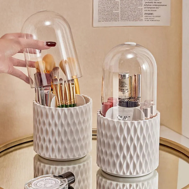 White acrylic rotating makeup brush holder with transparent body and a grey dust cover on a desk.