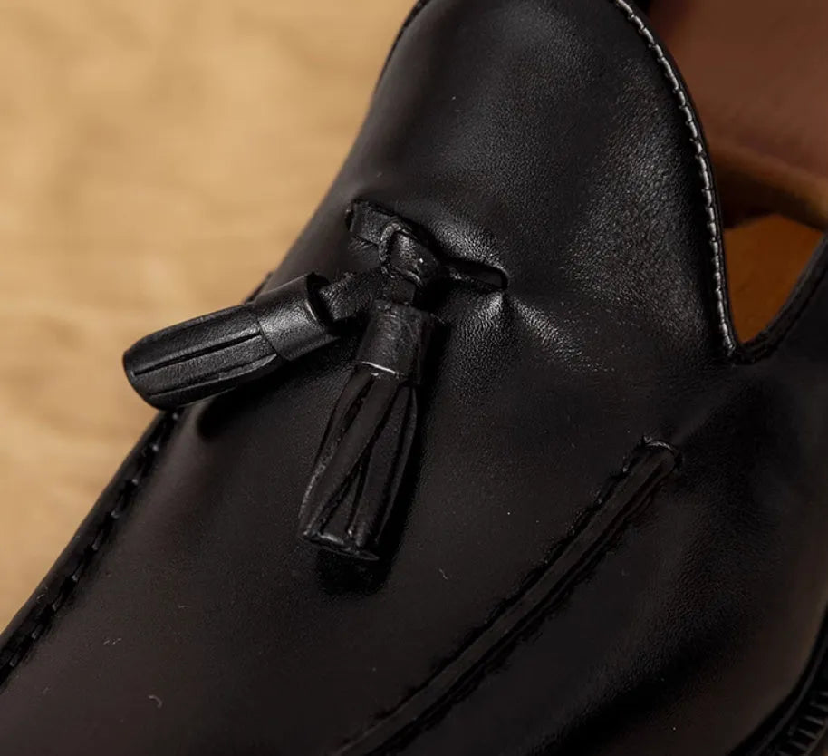 Men's black genuine leather slip-on loafers with fringed detailing and a rubber sole, shown from a side view.