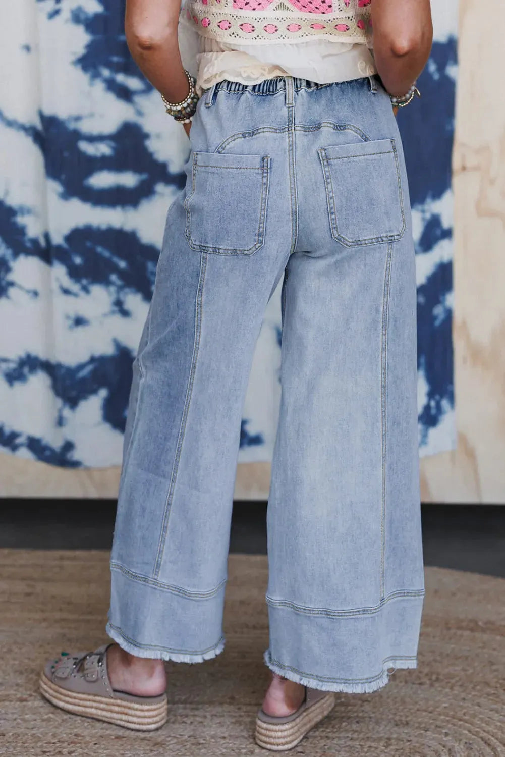 Beau blue women's wide leg denim trousers with a drawstring waistband and raw hem detail laid flat.