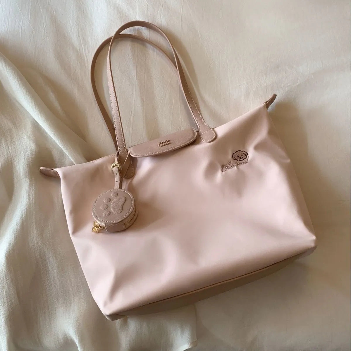 Women's large beige tote shoulder bag with external pockets and a horizontal square shape.