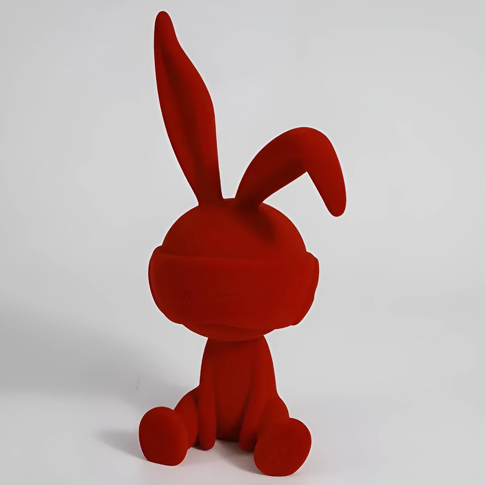Suede blindfold rabbit resin ornament in green, blue, or red colours on a shelf.