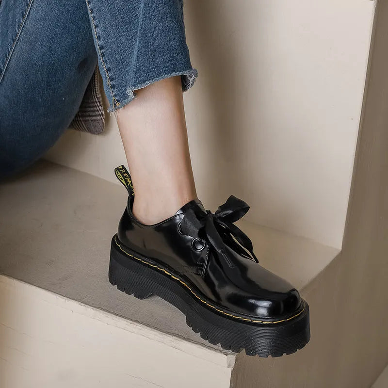 Women's black thick-soled leather-style lace-up shoes with ribbon and cross strap details on a white background.