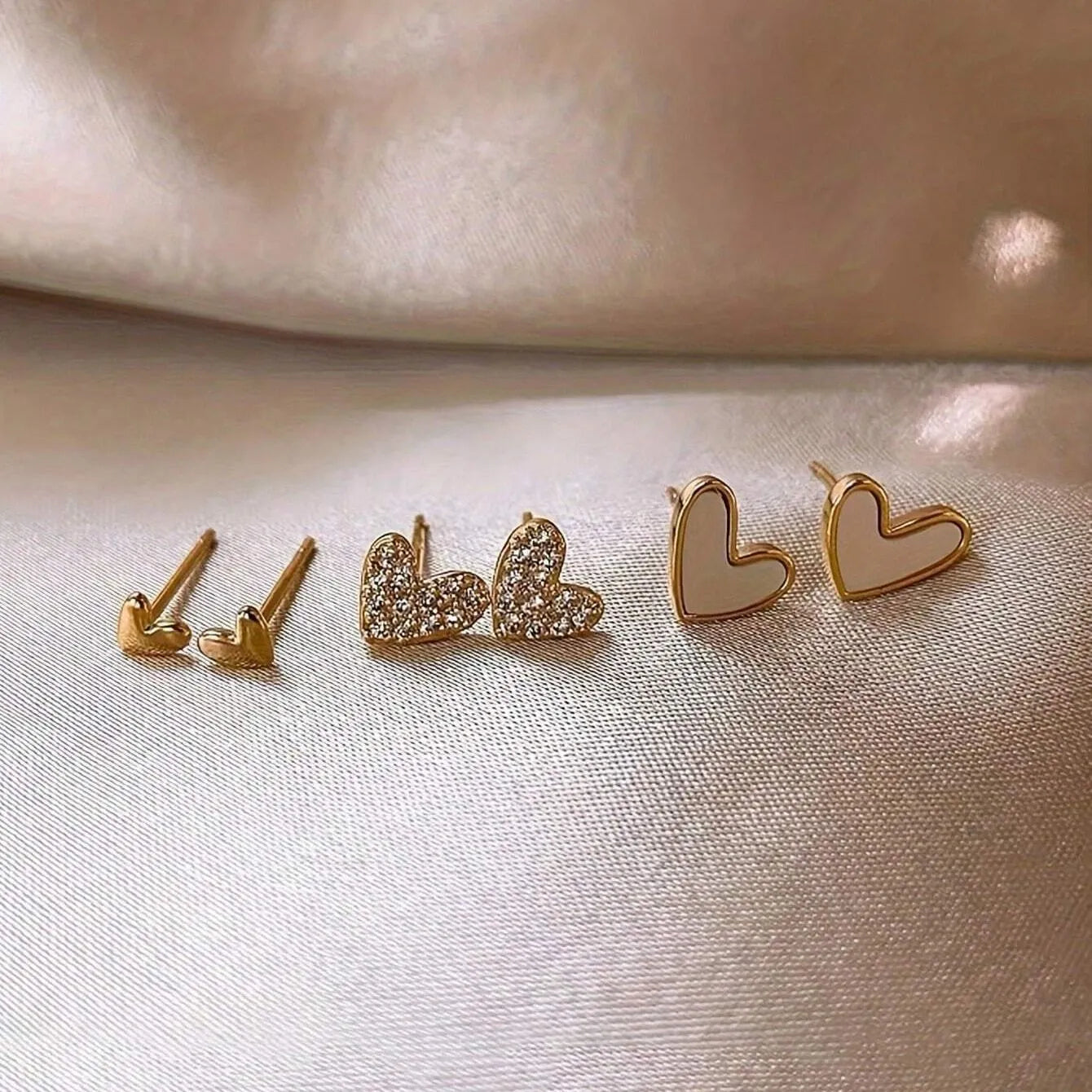 Set of three pairs of heart-shaped alloy earrings in gold, black, black and white, and pink colours.