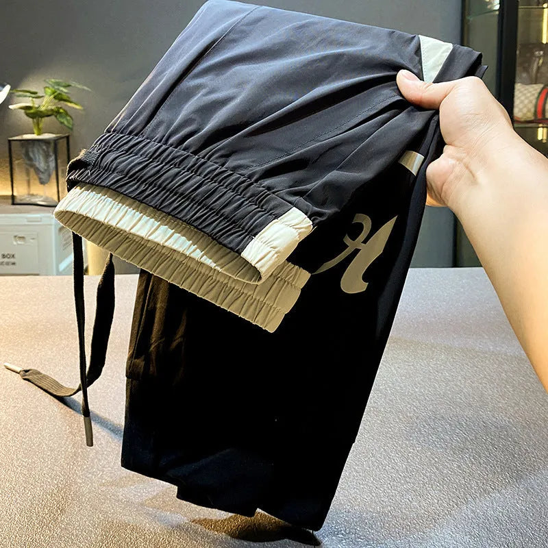 Men's solid black ultra-thin ice silk ankle-banded cropped casual trousers laid flat.