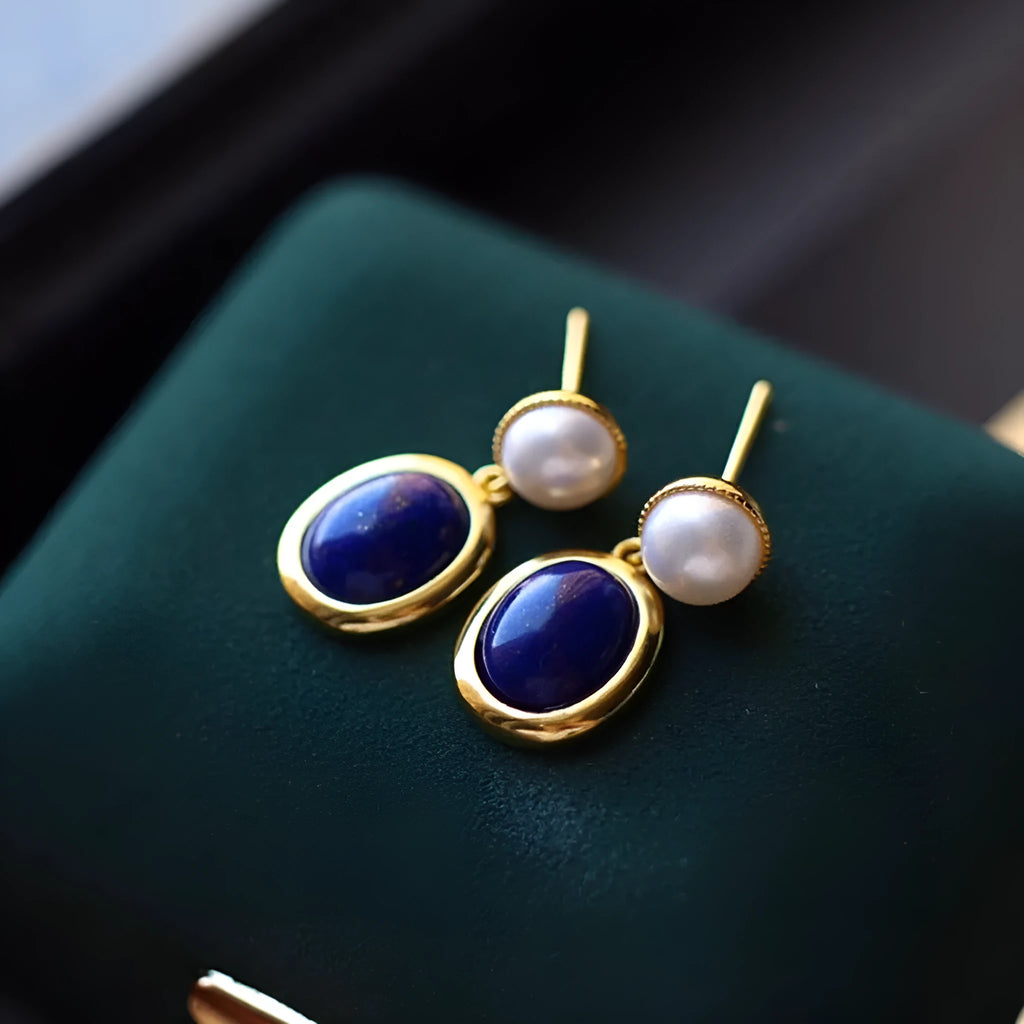 A pair of simple silver drop earrings with blue lapis lazuli pearls and auspicious pattern detailing.