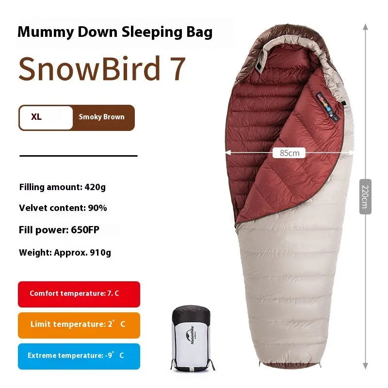 Adult mummy-style goose down sleeping bag in its storage bag, shown in a camping setting.