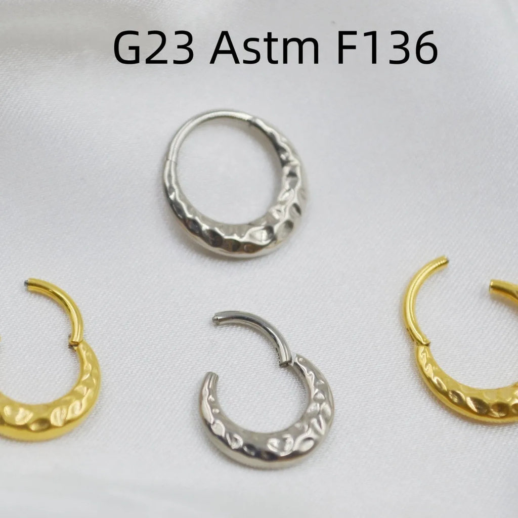 Close-up of a titanium alloy concave-convex nose ring in gold finish, showing detailed carving texture.