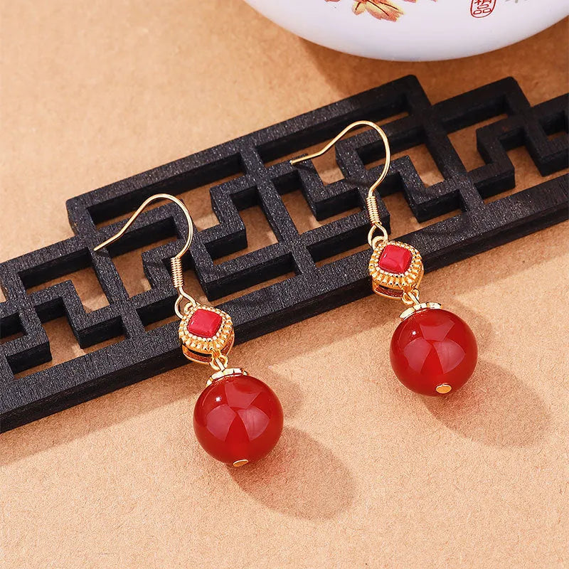 Round red agate bead drop earrings with silver-inlaid jasper accents on a geometric copper alloy hook.
