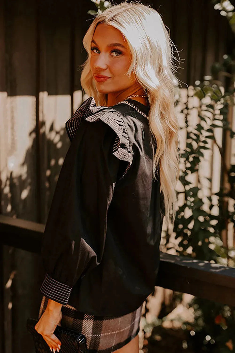 Black women's V-neck blouse with long ruffle sleeves and white contrast stitching.