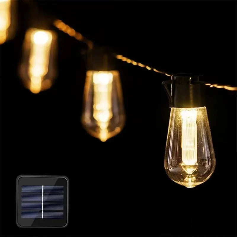Retro infusion bottle shaped glass bulb outdoor fairy lights with green cable, shown in garden setting.
